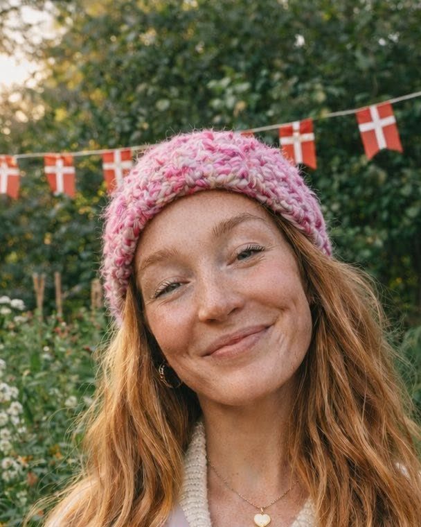 Tine, smilende udendørs i en varm strikhue